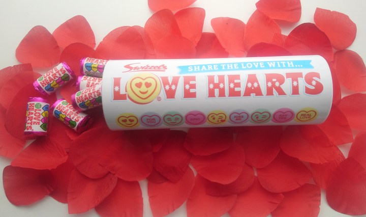 A tube of sweets on a bed of rose petals, with some packets of sweets pouring out.